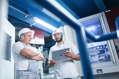Zwei Mitarbeiter in Arbeitskleidung mit Tablet an einer Anlage