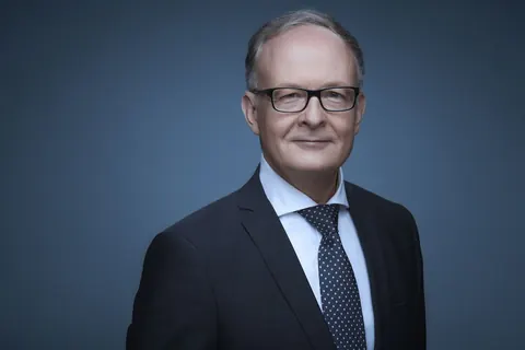 Mann mit Brille im dunklen Anzug vor blauem Hintergrund