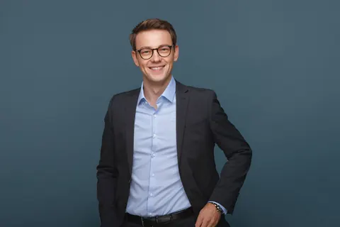 Mann mit Brille vor blaugrauem Hintergrund