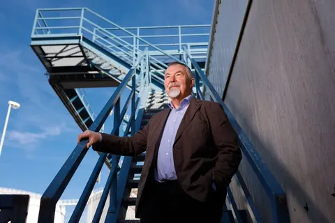 Mann im Sakko an einer Industrietreppe unter blauem Himmel