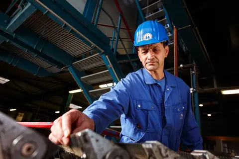 Mitarbeiter mit Schutzhelm an einer Maschine in der Werkhalle