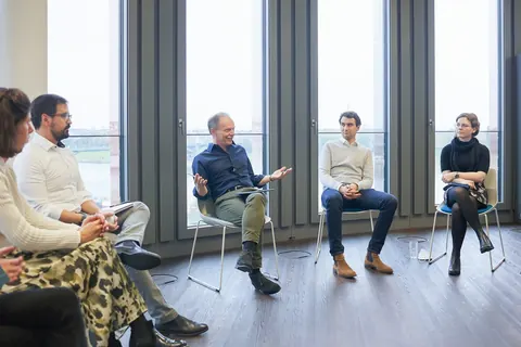 Team im Stuhlkreis bei einem Workshop vor großen Fenstern